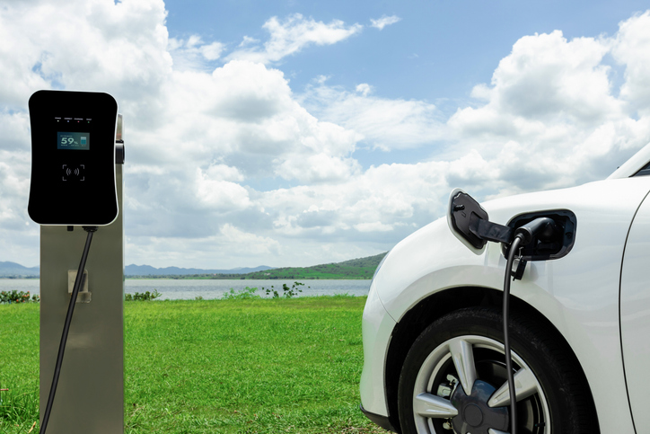 Progressive Concept Of Ev Car With Green Field, Hill And Lake As Background.